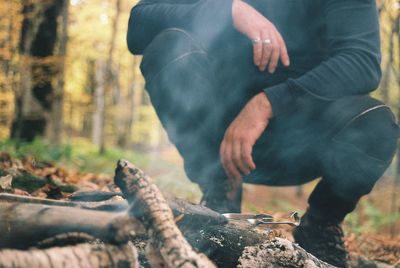 Low section of man crouching by campfire in forest