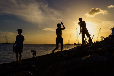 Silhouette people on beach against sky during sunset