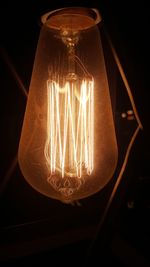 Close-up of illuminated light bulb hanging against black background