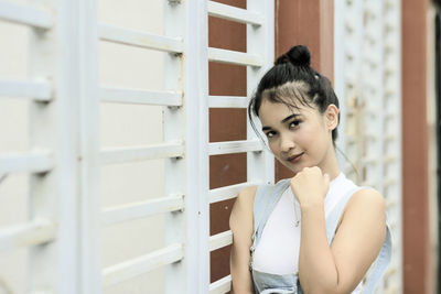 Portrait of beautiful woman with hand on chin standing by wall