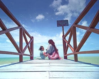 People sitting on bridge against sky