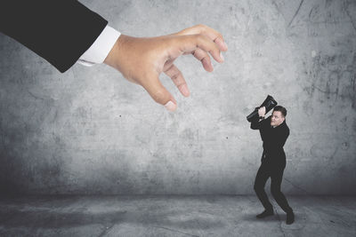 Digital composite image of cropped hand reaching towards businessman against wall