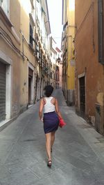 Rear view of woman walking on alley amidst buildings