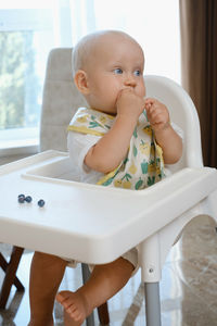 Baby boy eating berries in a high chair with bib. cute child having healthy snack on the kitchen