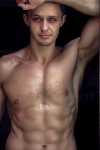 Portrait of shirtless young man standing against black background