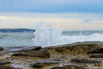 Close-up of wave splashing on beach against sky