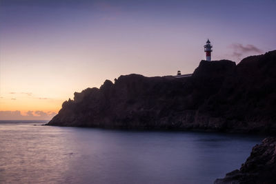 Lighthouse by sea against sky during sunset