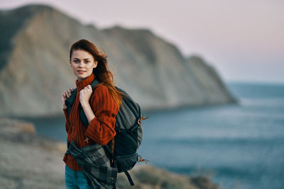 Portrait of young woman standing at beach against sky