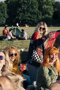 Smiling friends enjoying drink while camping on sunny day in concert