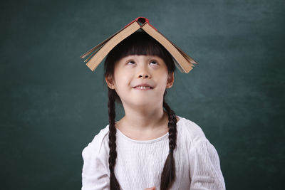 Girl with book on head standing by blackboard