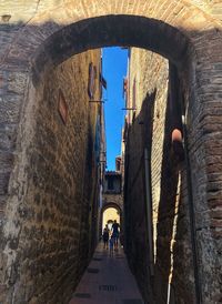 Rear view of people walking in alley amidst buildings in city