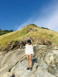 Rear view of woman standing on rock against sky