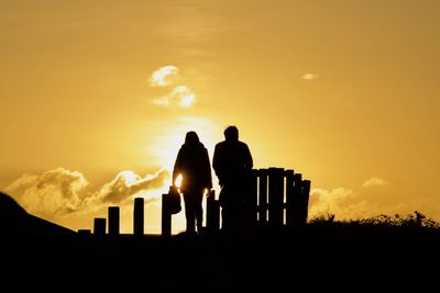 Silhouette men standing on field against sky during sunset