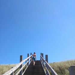 Rear view of man on footbridge against clear blue sky