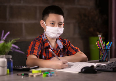 Happy boy studying with face mask on table at home