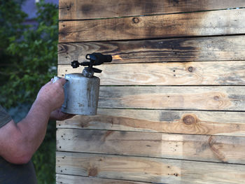 Cropped hand of man burning wooden plank outdoors