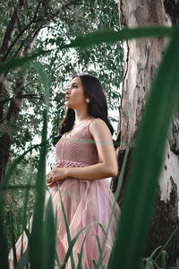 Side view of woman standing by tree against plants