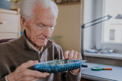 Smiling man holding seedlings in tray at home