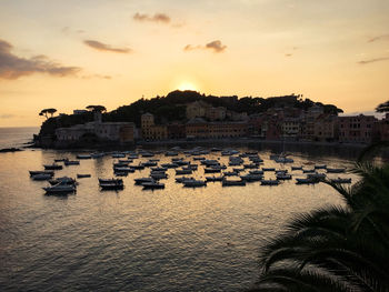 Boats in sea against buildings in city at sunset