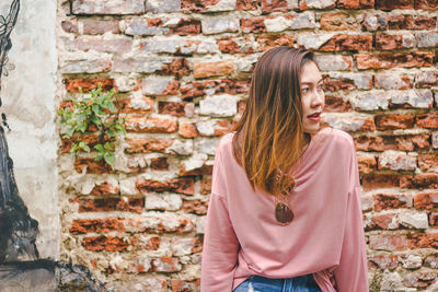 Young woman standing against brick wall