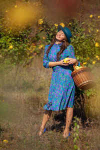 Full length of woman holding basket while standing by plants