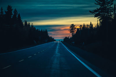 Empty road along silhouette trees at sunset