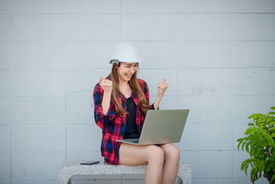 Young woman using mobile phone while sitting on wall