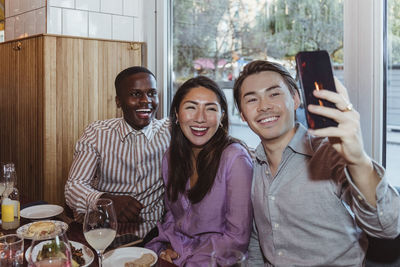 Cheerful male and female friends taking selfie on smart phone at restaurant