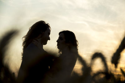 Silhouette couple at farm against sky during sunset