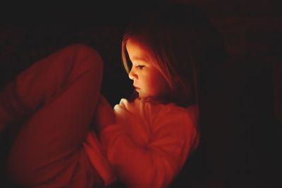 Side view of girl using mobile phone while lying in darkroom