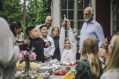 Happy boy with arms raised holding giraffe figurine by family during birthday celebration