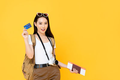 Portrait of smiling young woman standing against yellow background