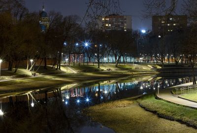 Illuminated street by lake in city at night