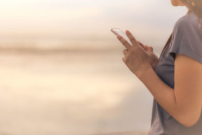 Midsection of woman using smart phone against sky during sunset