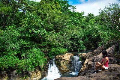 Woman sitting on rock by trees in forest