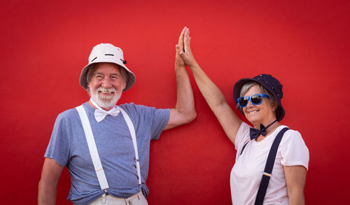 Senior couple high-fiving while standing against red wall