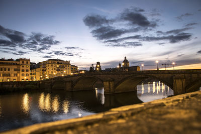 Bridge over river by buildings against sky