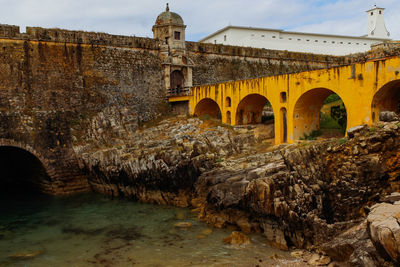 Arch bridge over beach by old building against sky in peniche fort