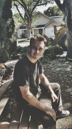 Portrait of young man sitting in yard against building