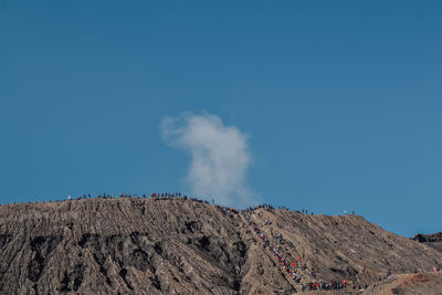 Low angle view of smoke emitting from volcanic mountain against blue sky