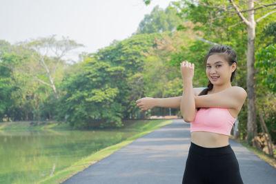 Portrait of young woman exercising on road by river at park