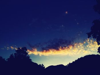 Low angle view of silhouette trees against blue sky