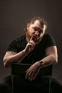 Young man sitting on chair against black background