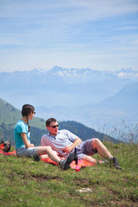 Friends sitting on mountain against sky