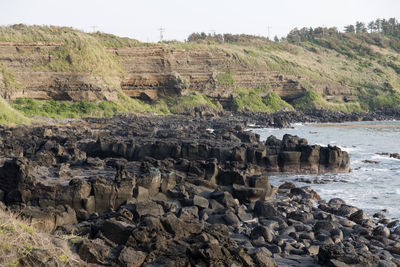 Rock formations by cliff against sky