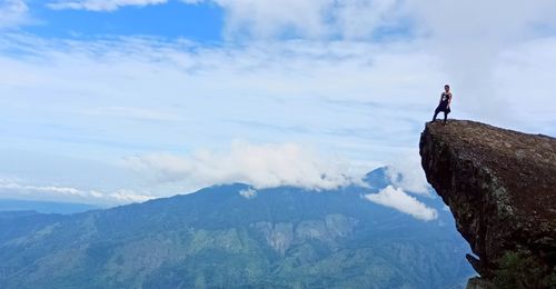 Man standing on rock looking at mountains against sky