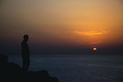 Silhouette man standing by sea against sky during sunset