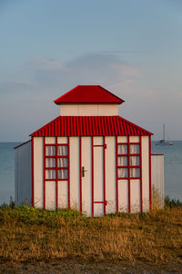 Red house on beach by sea against sky