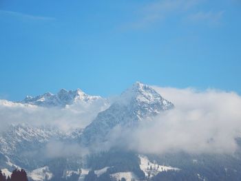 Snow covered rocky mountain against blue sky