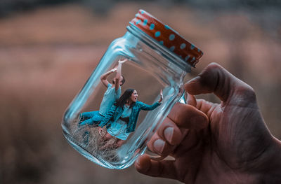 Cropped image of hand holding jar with people trapped in it